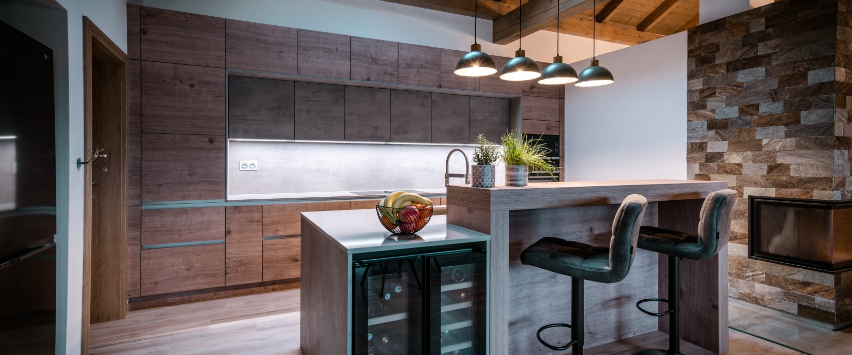 Detailní záběr na kuchyňský ostrůvek s integrovanou vinotékou, dřevěným barovým pultem a designovým osvětlením.