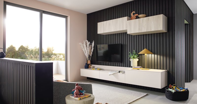 Bílá závěsná TV sestava a horní skříňky v dekoru dřeva instalované na elegantní černé stěně s vertikálním dřevěným lamelovým obkladem.