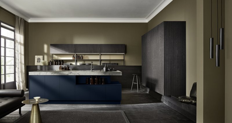 Architektonický celkový pohled na kuchyň Nolte neoCHALET v drážkovaném dubu Eiche Mokka s tmavě modrým ostrůvkem Soft Lack Tiefblau a mramorovou deskou.