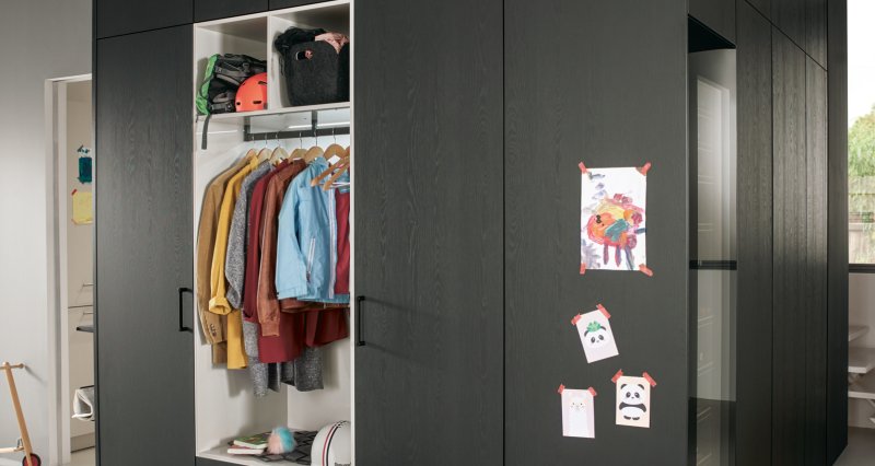 Černá matná vestavná skříň do předsíně na míru s otevřeným světlým modulem pro zavěšení bund a prostorem pro uložení tašek.