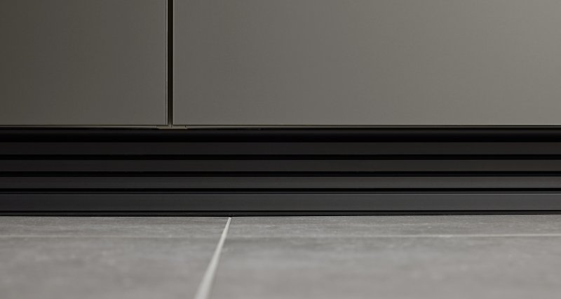Detailní pohled na černý drážkovaný sokl kuchyně Nolte Pearl elegantně navazující na šedou podlahovou dlažbu.