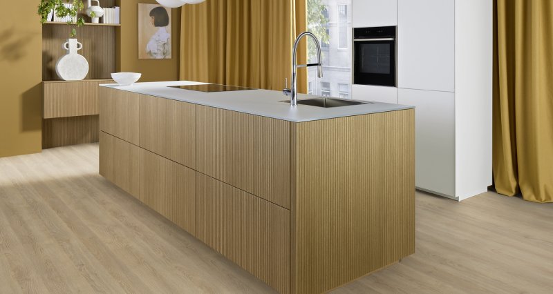 Boční pohled na kuchyňský ostrůvek v provedení světlého dubu s tenkou skleněnou pracovní deskou Glas Tec Satin v bílé barvě.