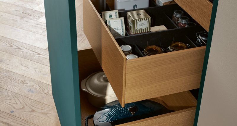 Otevřené plnovýsuvné kuchyňské zásuvky odhalující elegantní dřevěné rámy vnitřního systému Woodbox pro přehledné uložení zásob a nádobí.