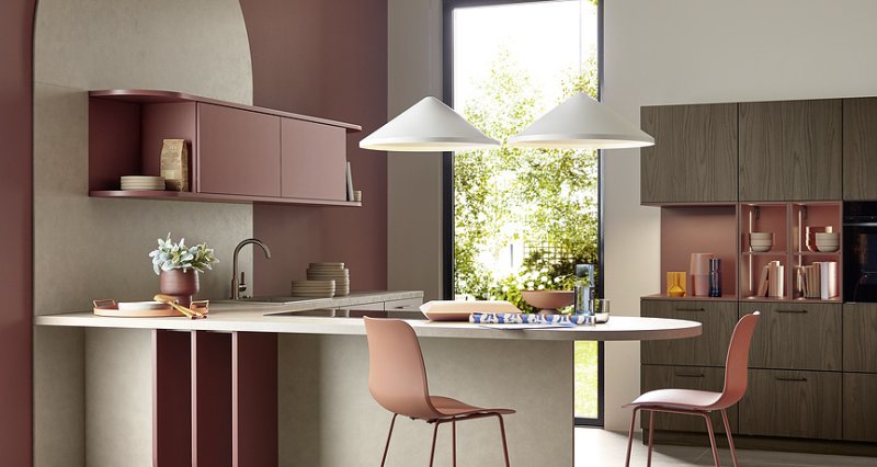 Kuchyňský ostrůvek Nolte se zakulacenou pracovní deskou, červenými barovými židlemi a designovým klenutým zádovým panelem v barvě Hennarot.