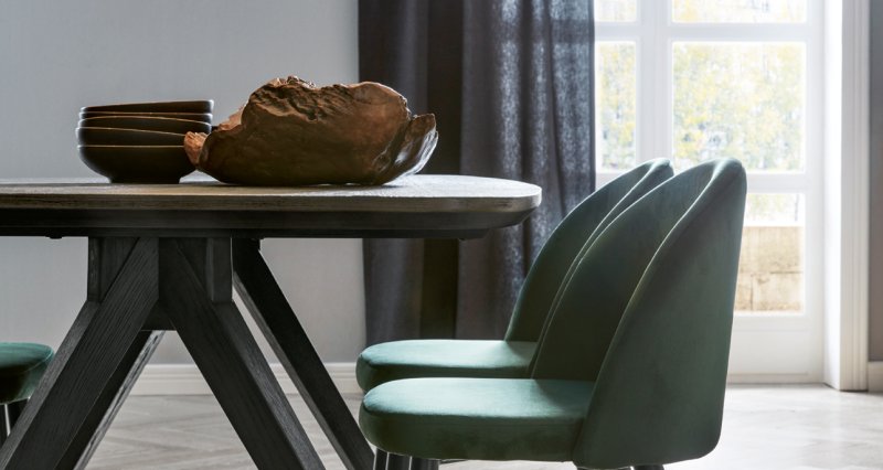 Detail moderního jídelního stolu s tmavou konstrukcí a elegantními sametovými židlemi ve smaragdově zelené barvě