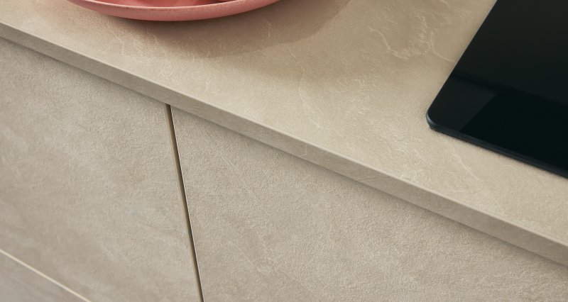Detail kamenné textury kuchyňské pracovní desky a čelních dvířek s růžovým talířem a citrony