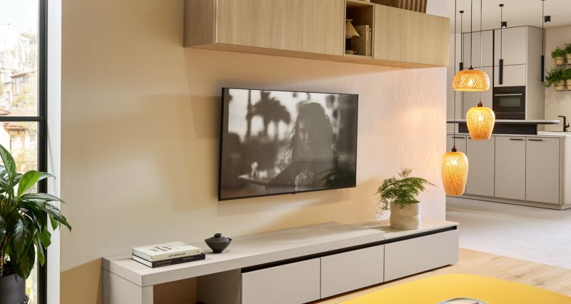 Čistý design obývací stěny tvořený krémovou bezúchytkovou TV komodou a horními závěsnými skříňkami v přírodním dřevěném dekoru.