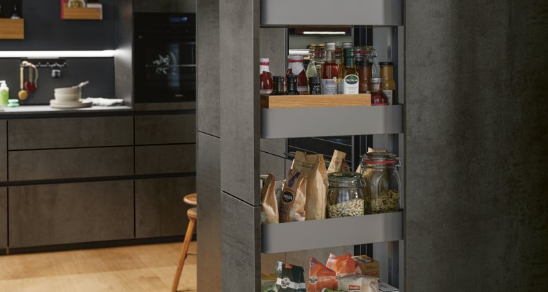 Detail otevřené vysoké potravinové skříně s hlubokými výsuvnými zásuvkami a organizéry v tmavém provedení