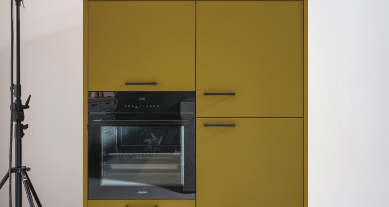 Detail designové vysoké kuchyňské skříně v hořčicově žlutém provedení s vestavnou horkovzdušnou troubou a černými úchytkami