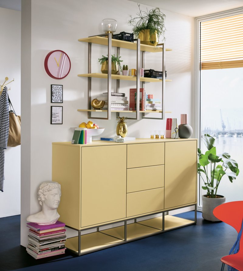 Žlutá úložná komoda a designový kovový regál s knihami a dekoracemi v obytném prostoru