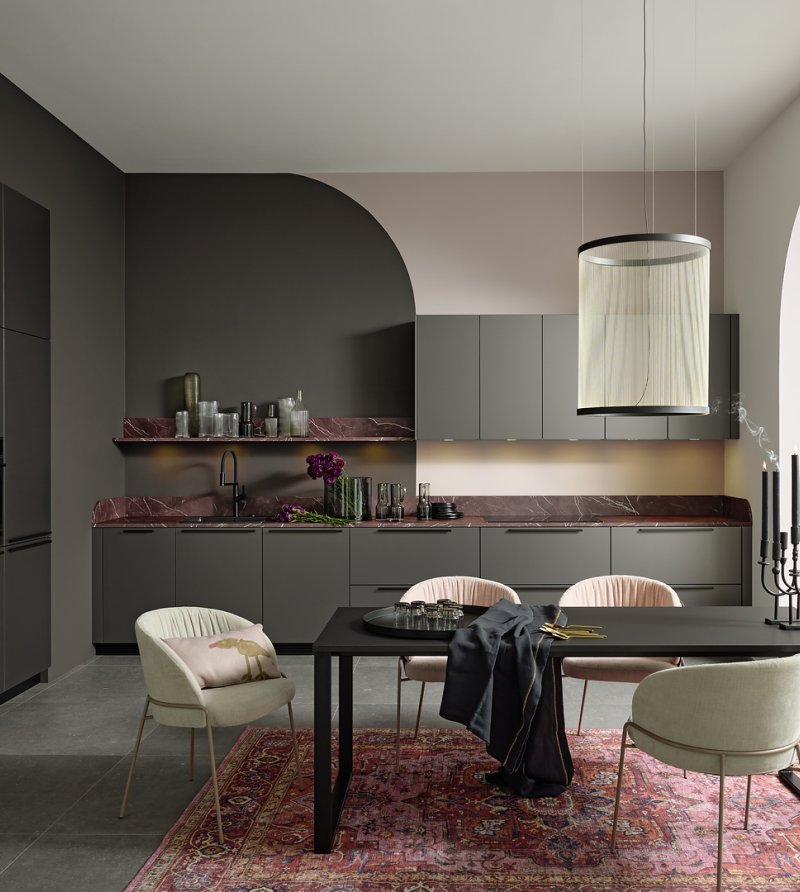 Celkový pohled na moderní šedou kuchyni Nolte Pearl Umbra metallic spojenou s jídelním koutem a výraznou pracovní deskou v dekoru červeného mramoru.