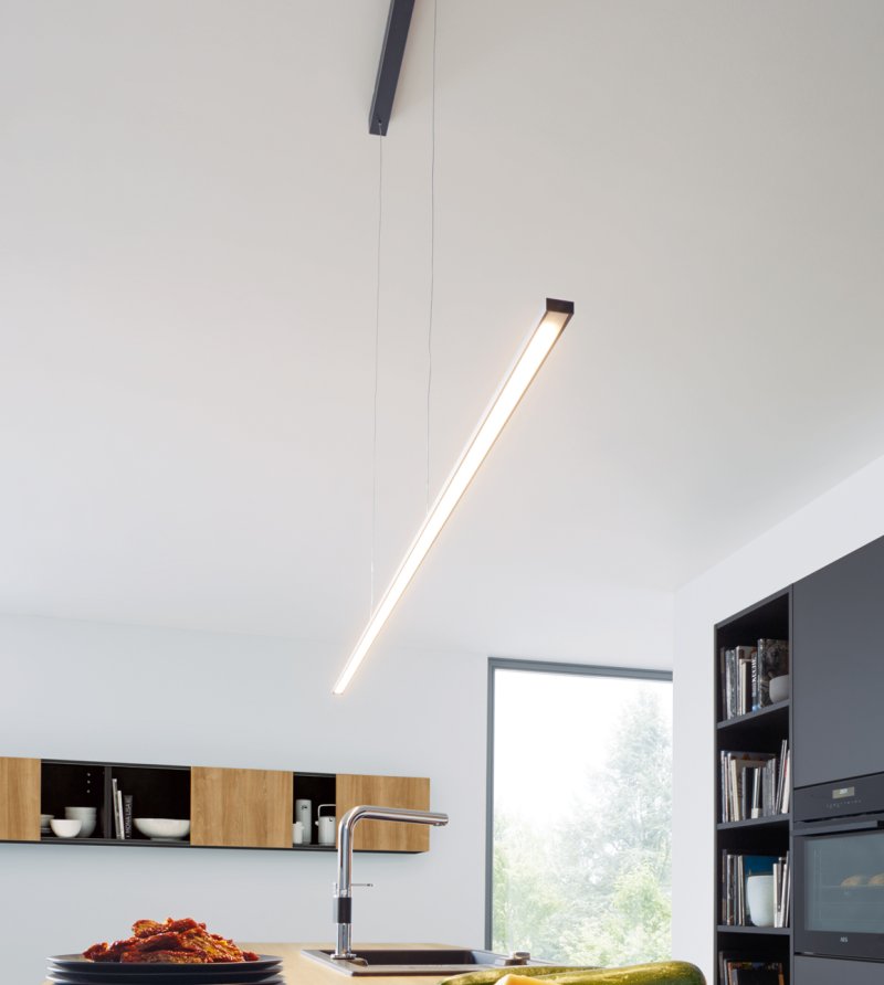 Detail minimalistického lineárního závěsného svítidla s teplým LED osvětlením nad dřevěnou deskou kuchyňského ostrůvku
