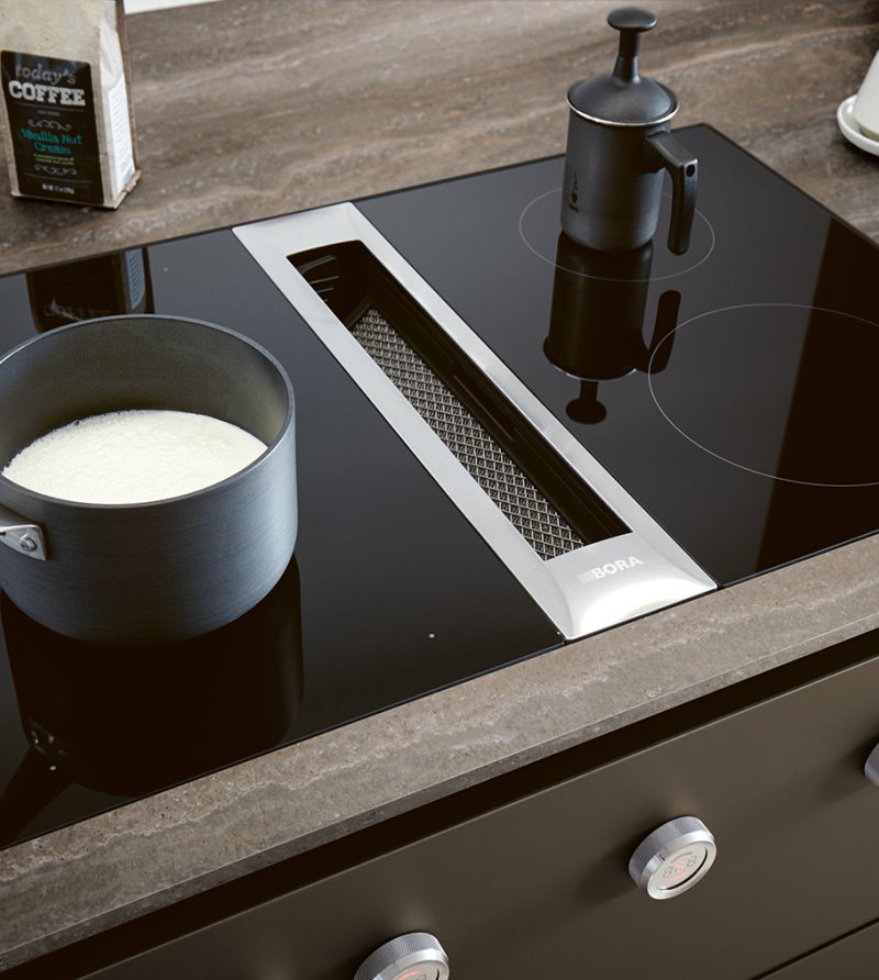 Detailní záběr na varnou desku zapuštěnou do pracovní desky Systemo Travertin dark v kuchyni Next125 NX912 spolu s ovládacími knoflíky.