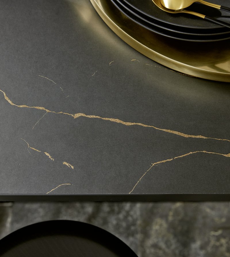 Detailní pohled na tmavou pracovní desku s výrazným zlatým žilkováním připomínajícím luxusní mramor v moderní kuchyni Nolte.