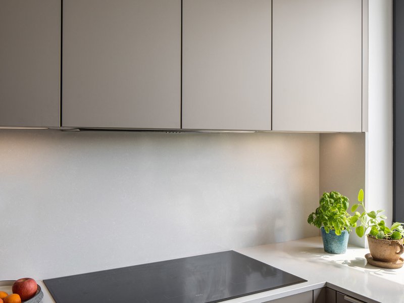 Detail varné zóny s moderní indukční deskou, čistou pracovní deskou, LED podsvícením a čerstvými bylinkami v květináčích.