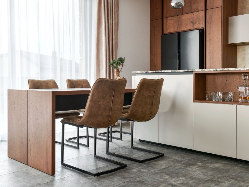 Zakázkový masivní jídelní stůl s čalouněnými židlemi na kovových podnožích navazující na designový kuchyňský ostrůvek.