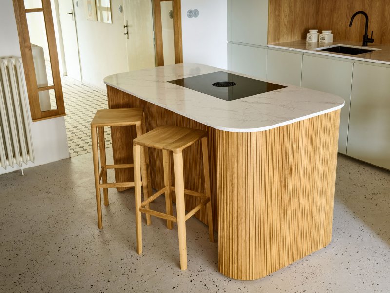 Detailní záběr na kuchyňský ostrůvek s lamelovým dekorem, kamennou deskou a moderní indukční varnou deskou s integrovaným odsavačem par.