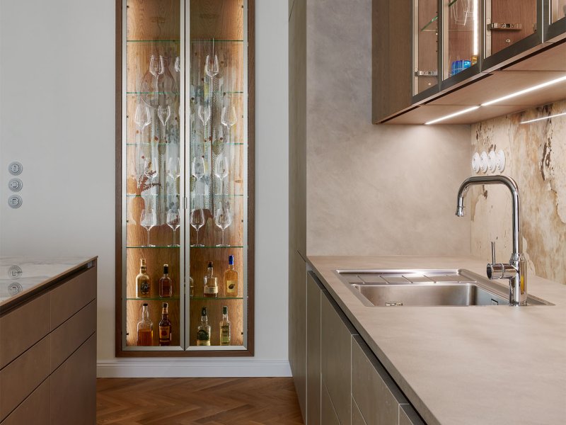 Detailní pohled na elegantní vysokou prosklenou vitrínu s vnitřním vertikálním osvětlením určenou pro uložení skleniček a lahví.