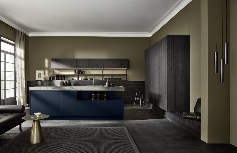 Architektonický celkový pohled na kuchyň Nolte neoCHALET v drážkovaném dubu Eiche Mokka s tmavě modrým ostrůvkem Soft Lack Tiefblau a mramorovou deskou.