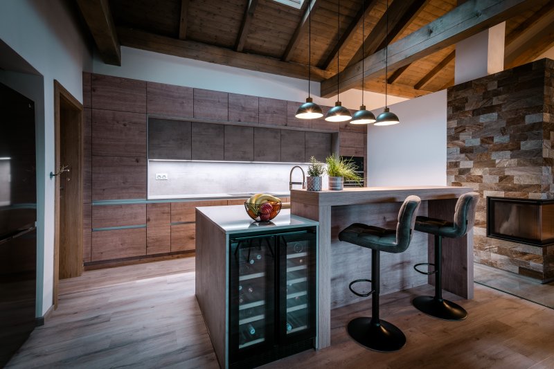 Detailní záběr na kuchyňský ostrůvek s integrovanou vinotékou, dřevěným barovým pultem a designovým osvětlením.