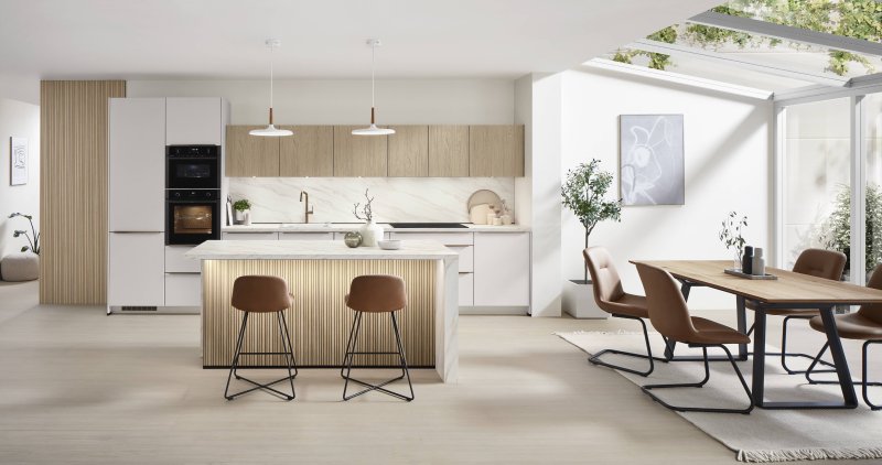 Velký celkový pohled na designovou kuchyni Nobilia Softline 509 v provedení bílá Perfect matná s mramorovou deskou Carrara Bronze a navazujícím jídelním stolem.
