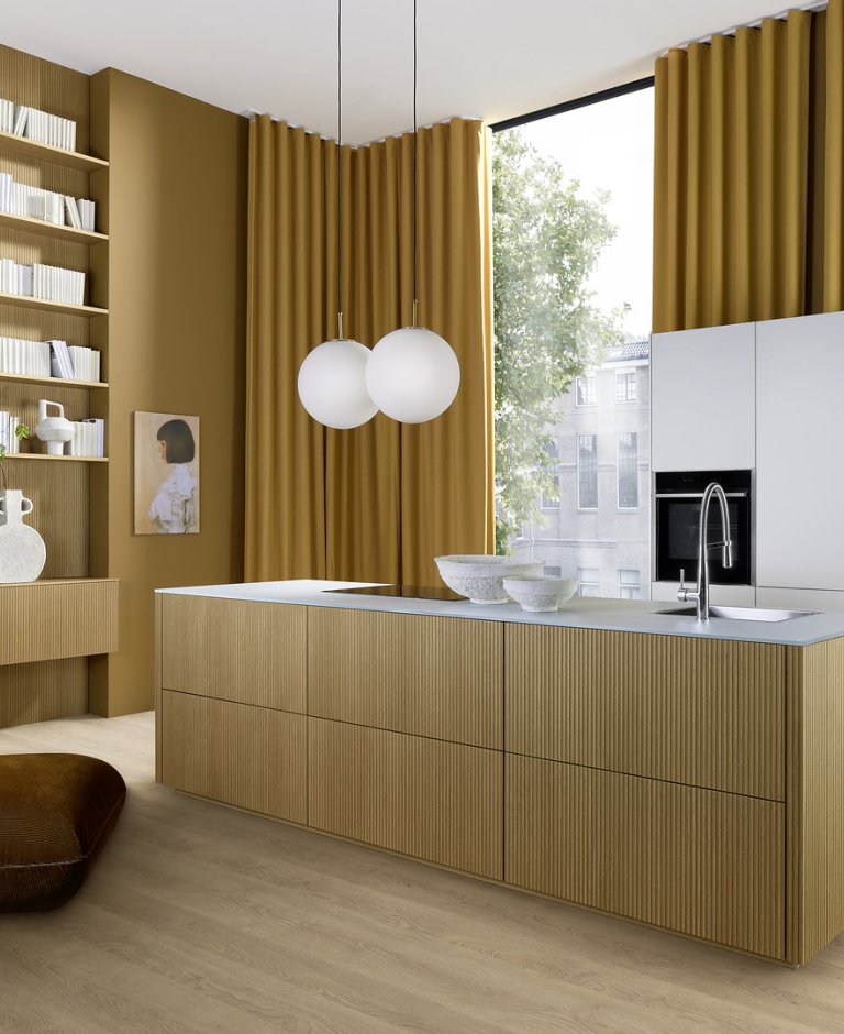 Prostorná kuchyně Nolte neo LODGE kombinující drážkovaný ostrůvek ze světlého dubu, pracovní desku Glas Tec Satin a vysoké bílé skříně.