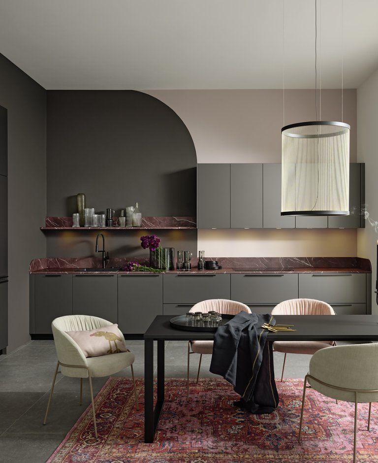 Celkový pohled na moderní šedou kuchyni Nolte Pearl Umbra metallic spojenou s jídelním koutem a výraznou pracovní deskou v dekoru červeného mramoru.