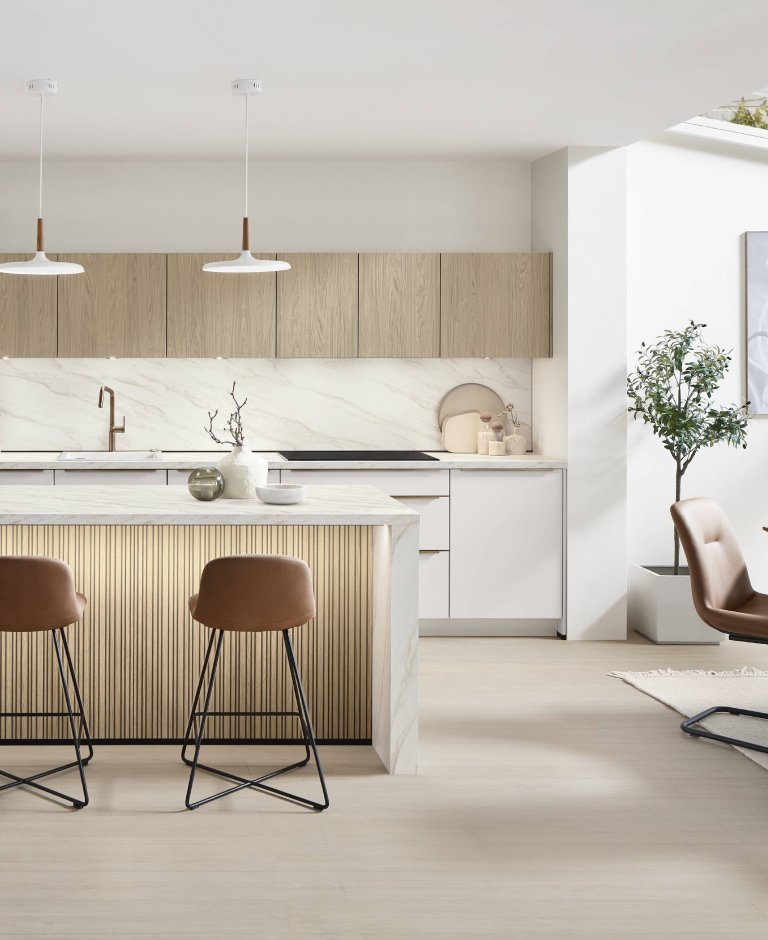 Velký celkový pohled na designovou kuchyni Nobilia Softline 509 v provedení bílá Perfect matná s mramorovou deskou Carrara Bronze a navazujícím jídelním stolem.