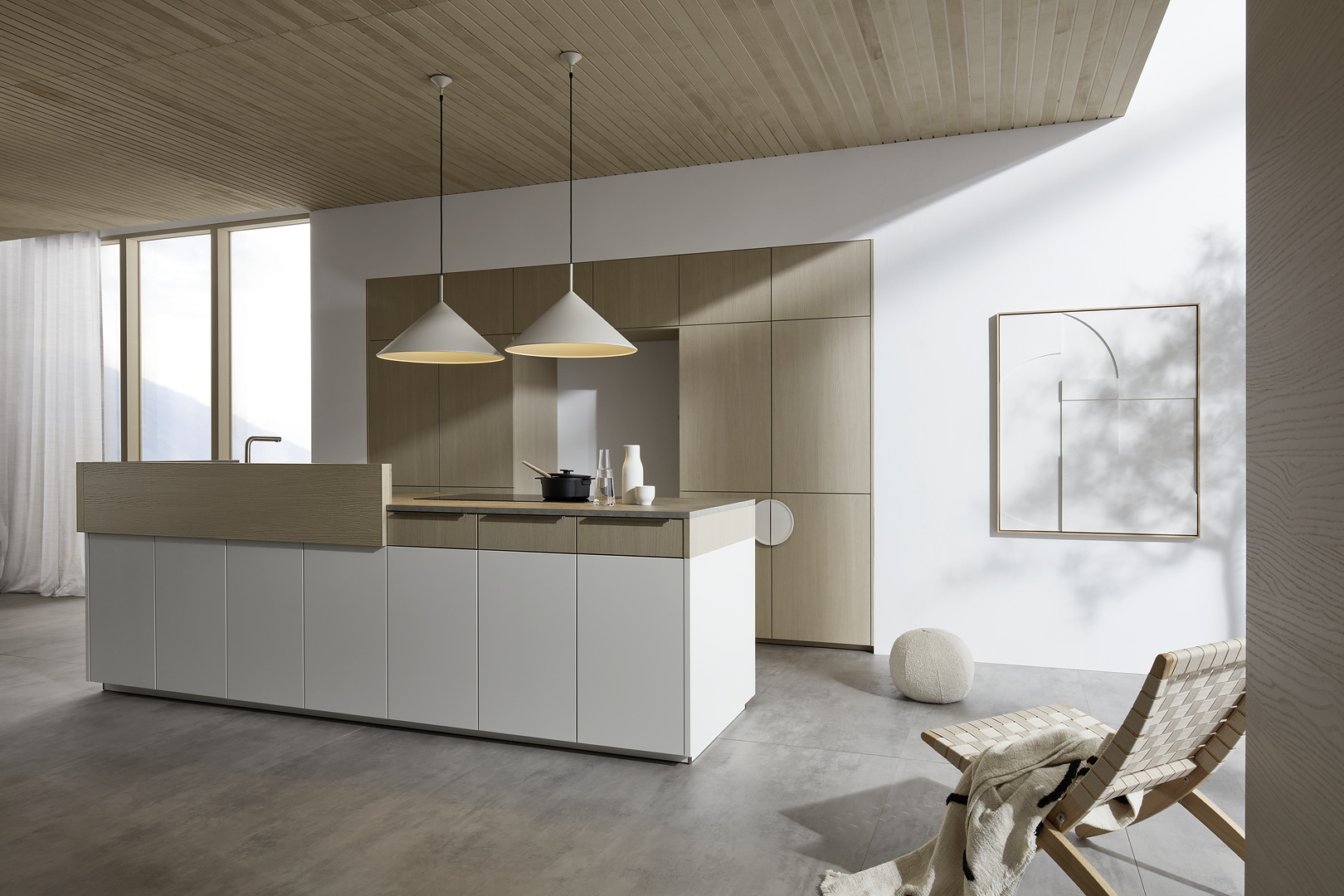 Širokoúhlá perspektiva kuchyně Nolte neo Leaf v kombinaci bílé matné barvy a jasanu pískového s designovým křeslem v popředí.