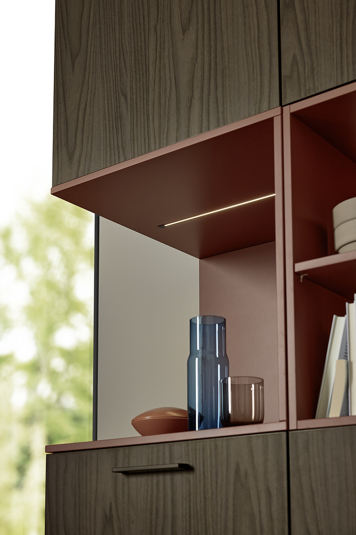 Detailní pohled na otevřenou niku v barvě Hennarot zabudovanou do dřevěných skříní s elegantním zafrézovaným LED osvětlením.