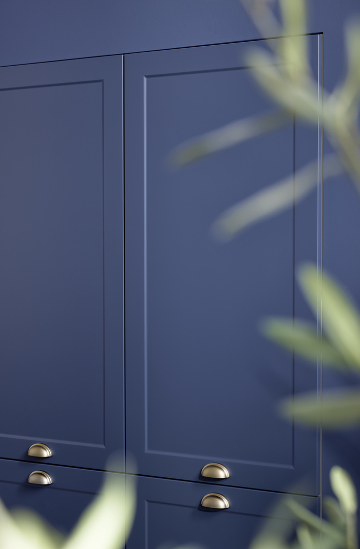 Detailní záběr na modrá rámečková dvířka kuchyně Nolte Ravenna v barvě Blaubeere s elegantními kovovými mušlovými úchytkami.